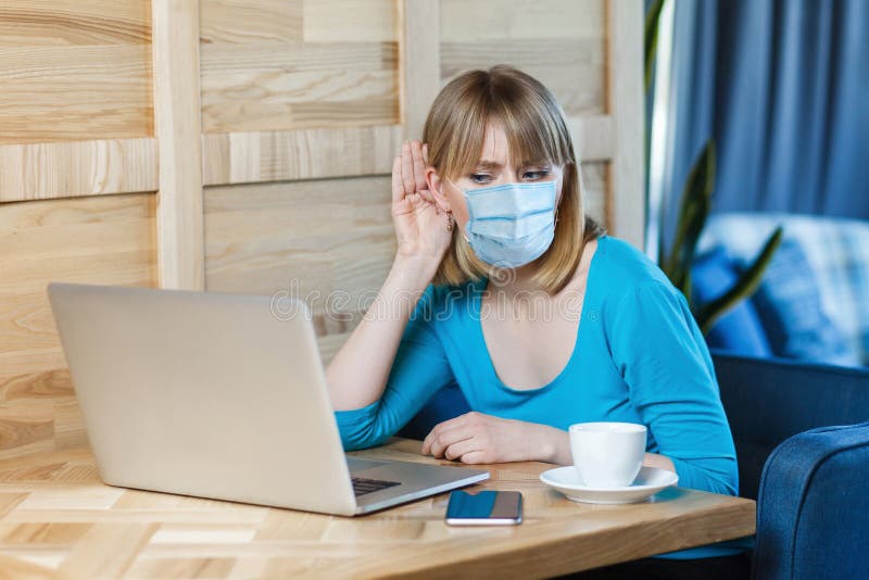 Le portrait de la jeune femme attentive avec le masque médical chirurgical est assis et travaillant sur l'ordinateur portable et j photographie stock