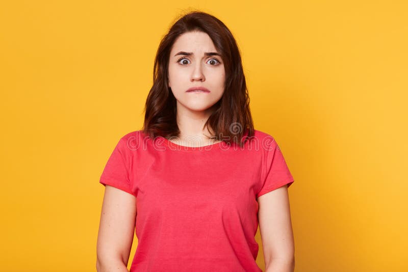 Le portrait de la jeune jolie femme émotive sur le fond jaune, mord sa lèvre, regarde la caméra avec l'expression du visage effra photographie stock Le portrait de la jeune jolie femme émotive sur le fond jaune, mord sa lèvre, regarde la caméra avec l'expression du visage effra photographie stock