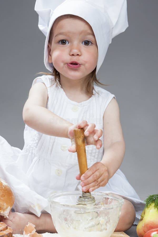 Le portrait de la petite fille caucasienne dans le cuisinier Uniform Working With battent photo stock Le portrait de la petite fille caucasienne dans le cuisinier Uniform Working With battent photo stock