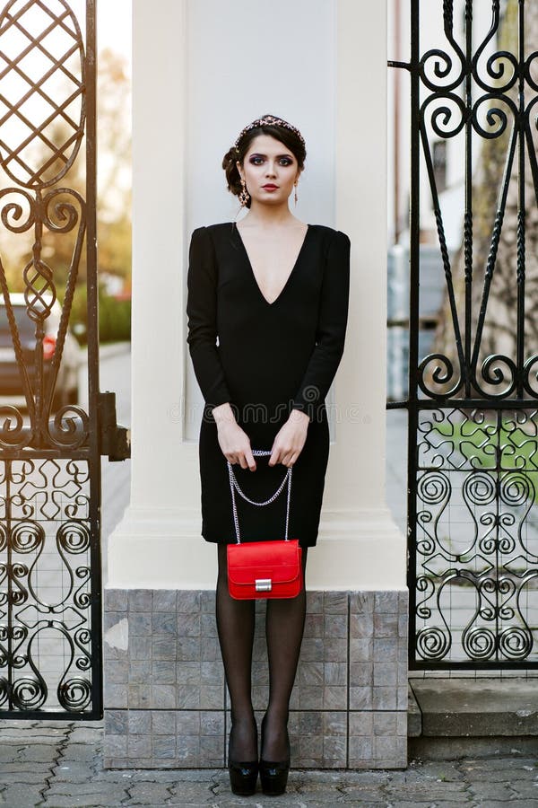 Le portrait de mode de vie de la jeune femme élégante entre dans la ville avec un sac à la mode rouge Sur le sac d'embrayage d'ép image stock Le portrait de mode de vie de la jeune femme élégante entre dans la ville avec un sac à la mode rouge Sur le sac d'embrayage d'ép image stock