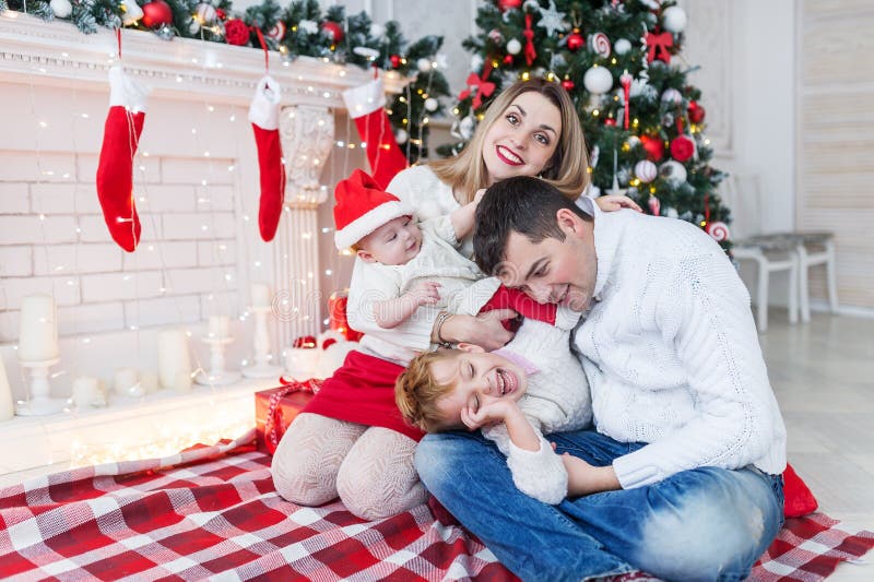 Le portrait de plan rapproché de la famille gaie mignonne près de l'arbre de Noël à la maison, les parents heureux avec des enfan photo stock Le portrait de plan rapproché de la famille gaie mignonne près de l'arbre de Noël à la maison, les parents heureux avec des enfan photo stock
