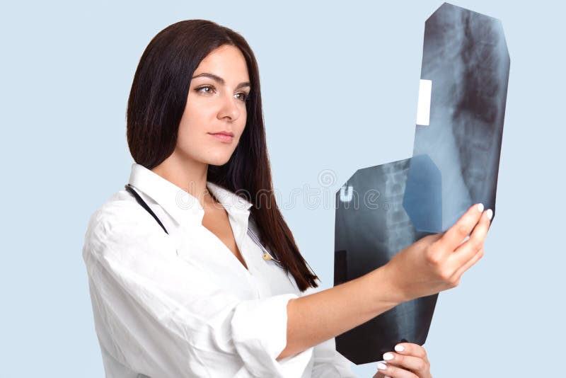 Le portrait du jeune spécialiste féminin attirant dans la sphère de radiologie étudie des rayons de X de squelette humain du ` s, images libres de droits Le portrait du jeune spécialiste féminin attirant dans la sphère de radiologie étudie des rayons de X de squelette humain du ` s, images libres de droits