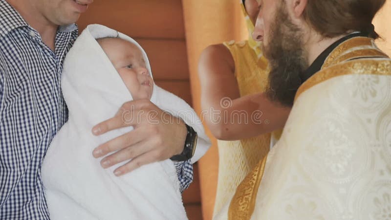 Le prêtre habille une serviette sur le petit bébé après une cérémonie de baptême dans l'eau sainte