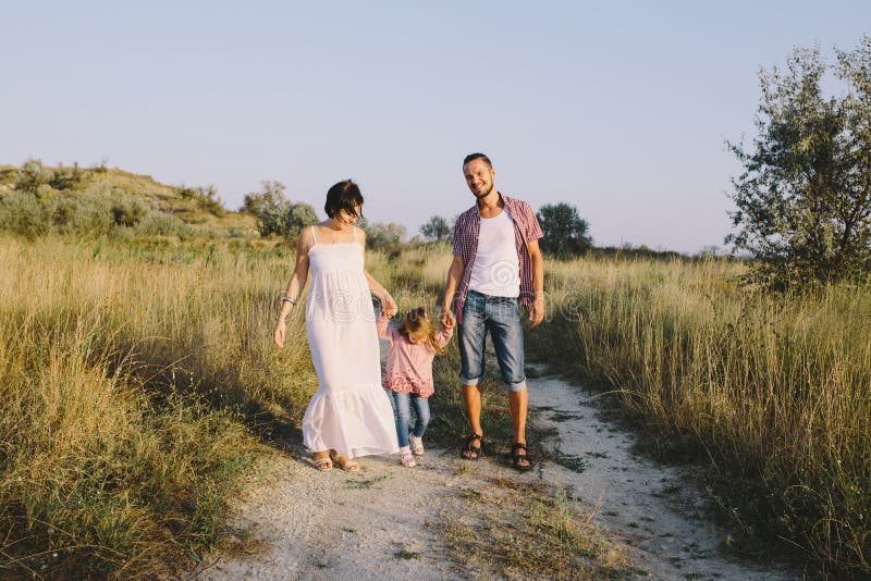 Le père et la mère enceinte mène sa fille par la main extérieure image stock Le père et la mère enceinte mène sa fille par la main extérieure image stock