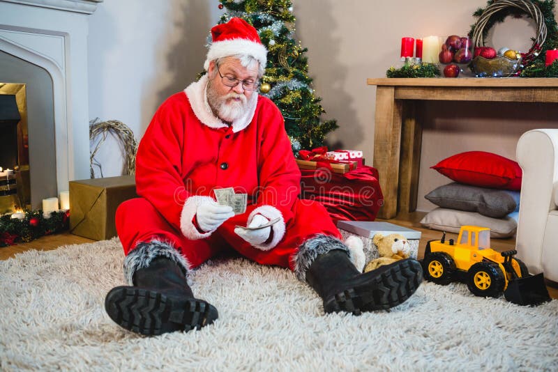Le père noël s'asseyant sur le plancher et comptant l'argent liquide photo stock Le père noël s'asseyant sur le plancher et comptant l'argent liquide photo stock