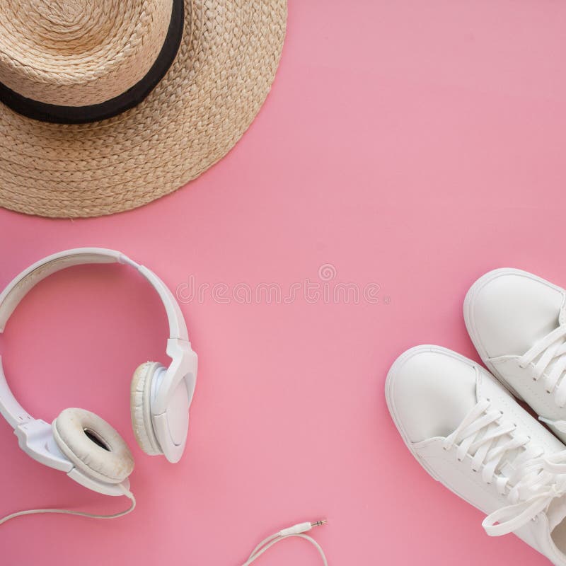 Le scarpe da tennis bianche, il cappello di paglia, cuffie, stanno trovando su un fondo rosa luminoso fotografia stock Le scarpe da tennis bianche, il cappello di paglia, cuffie, stanno trovando su un fondo rosa luminoso fotografia stock