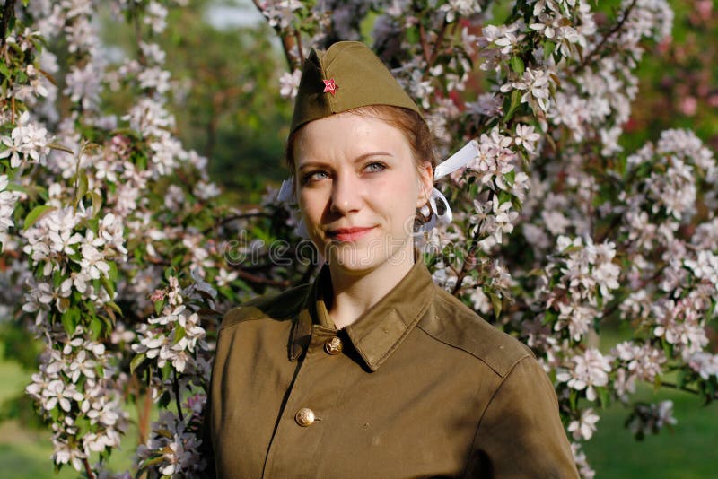 Le soldat féminin soviétique dans l'uniforme de la deuxième guerre mondiale se tient près de l'arbre fleurissant photos libres de droits Le soldat féminin soviétique dans l'uniforme de la deuxième guerre mondiale se tient près de l'arbre fleurissant photos libres de droits