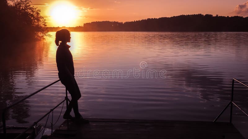 Le soleil de fond de fille de silhouette Fille tenant l'eau proche dehors Lac de coucher du soleil d'or Jeune femme pensant à que photos libres de droits Le soleil de fond de fille de silhouette Fille tenant l'eau proche dehors Lac de coucher du soleil d'or Jeune femme pensant à que photos libres de droits