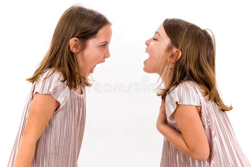 Identical twin girls sisters are arguing yelling at each other. Angry girls are shouting, yelling and arguing with emotional expression on faces. Frontal profile view of children. Isolated on white. Identical twin girls sisters are arguing yelling at each other. Angry girls are shouting, yelling and arguing with emotional expression on faces. Frontal profile view of children. Isolated on white