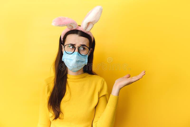 Le studio tiré de la femme en verres en utilisant les oreilles médicales de masque et de lapin soulève la paume comme si montrant images stock