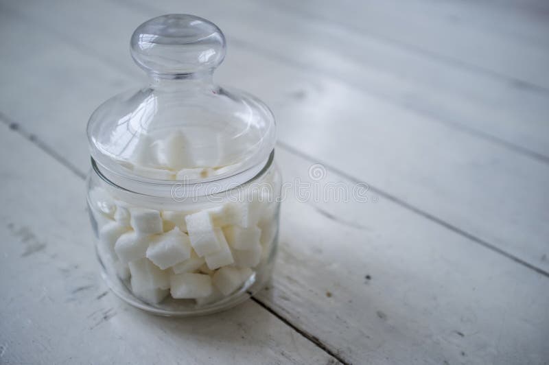 Le sucre blanc met en bloc dans un pot en verre sur la table en bois peinte dedans image stock Le sucre blanc met en bloc dans un pot en verre sur la table en bois peinte dedans image stock