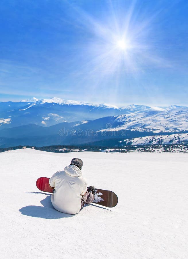 Le surfeur détendant contre des montagnes en soleil rayonne, des sports d'hiver où les vacances voyagent au concept de station th