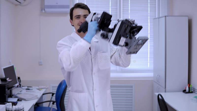 Le technicien de laboratoire de jeune homme danse dans le laboratoire avec des microscopes dans des mains