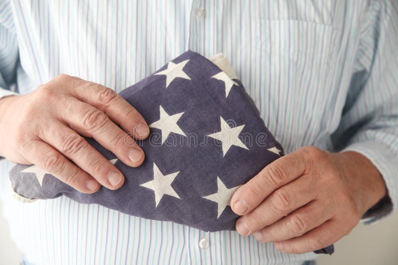 Le tenute dell'uomo hanno piegato la bandiera americana fotografie stock Le tenute dell'uomo hanno piegato la bandiera americana fotografie stock