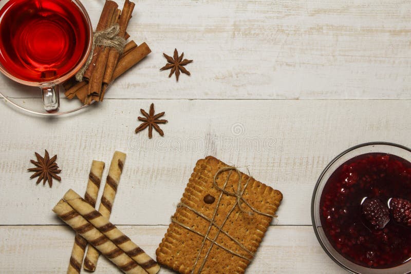 Le thé dans une tasse avec de la confiture de framboise, biscuits, croissants, cannelle, anis, caramel colle Sur une table en boi photo libre de droits Le thé dans une tasse avec de la confiture de framboise, biscuits, croissants, cannelle, anis, caramel colle Sur une table en boi photo libre de droits