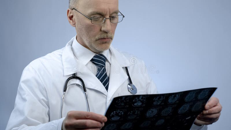 Le thérapeute masculin expérimenté regardant le balayage de cerveau de patients, vérifiant l'IRM résulte image stock Le thérapeute masculin expérimenté regardant le balayage de cerveau de patients, vérifiant l'IRM résulte image stock