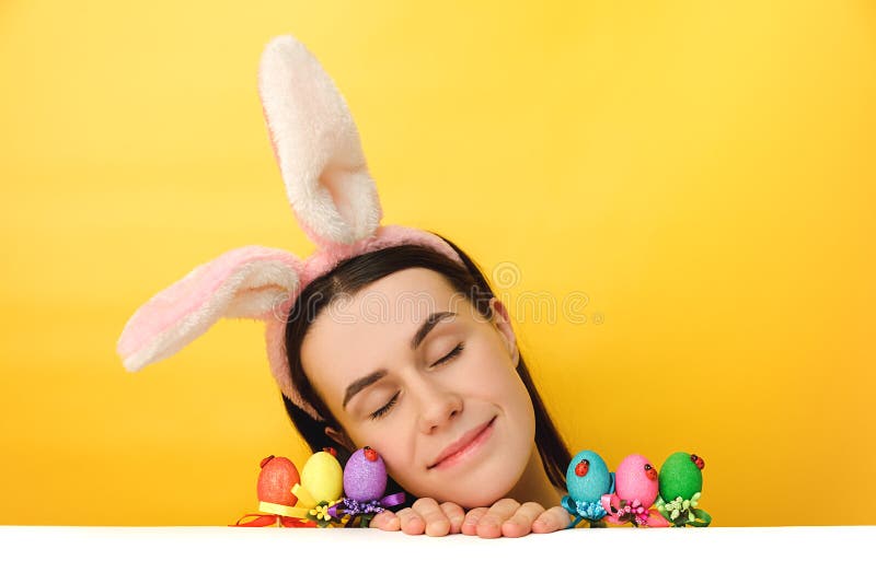 Le tir horizontal de la jolie femme siège au bureau avec les yeux fermés à proximité des oeufs de pâques colorés porte le visage p photographie stock