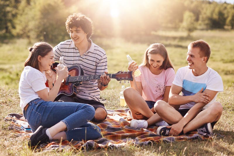 Le tir horizontal des jeunes amicaux ont l'amusement, passent le temps libre pendant le week-end ensemble, se reposent sur la ter photo libre de droits Le tir horizontal des jeunes amicaux ont l'amusement, passent le temps libre pendant le week-end ensemble, se reposent sur la ter photo libre de droits