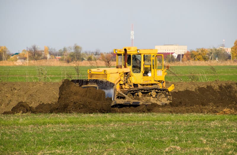 Le tracteur jaune avec le grederom joint fait la mise ? niveau de la terre photos stock Le tracteur jaune avec le grederom joint fait la mise ? niveau de la terre photos stock