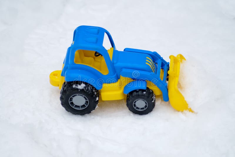 Children's toy tractor lies on the snow in the winter park-. Children's toy tractor lies on the snow in the winter park-