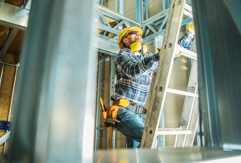 Skeleton Steel Building Construction Worker Wearing Safety Hard Hat and Noise Reduction Headphones. Going Up Using Ladder. Skeleton Steel Building Construction Worker Wearing Safety Hard Hat and Noise Reduction Headphones. Going Up Using Ladder