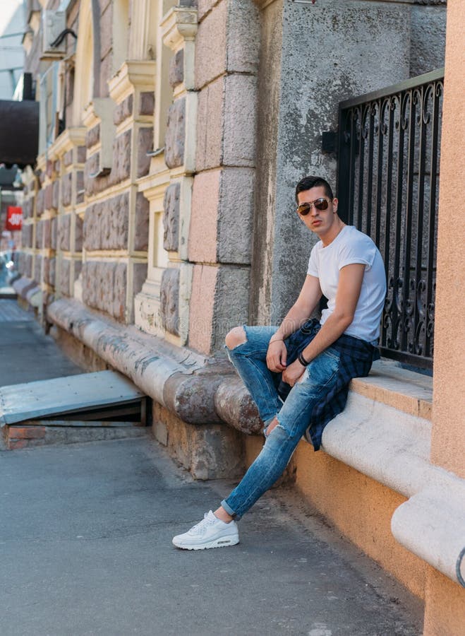 Le type attirant et sexy s'assied sur la rue dans des lunettes de soleil confiance en soi, flatulence et arrogance mod?le, posant images libres de droits Le type attirant et sexy s'assied sur la rue dans des lunettes de soleil confiance en soi, flatulence et arrogance mod?le, posant images libres de droits