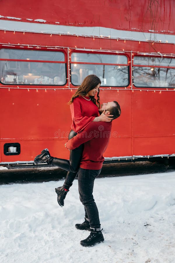 the guy lifted the girl in his arms and circles her against the background of a red bus. High quality photo. the guy lifted the girl in his arms and circles her against the background of a red bus. High quality photo