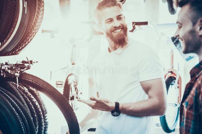Le vendeur aide le jeune acheteur à choisir des pneus pour la bicyclette photos libres de droits