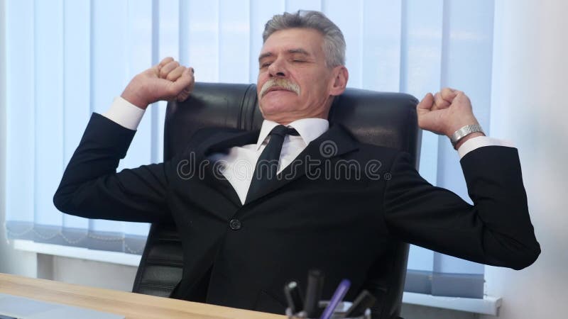 Le vieil homme d'affaires s'est penché de retour dans sa chaise de bureau, il sourient et rêvassant photo libre de droits Le vieil homme d'affaires s'est penché de retour dans sa chaise de bureau, il sourient et rêvassant photo libre de droits