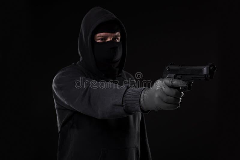 Le voleur dans un masque avec une arme à feu a indiqué le côté sur un fond noir images libres de droits Le voleur dans un masque avec une arme à feu a indiqué le côté sur un fond noir images libres de droits