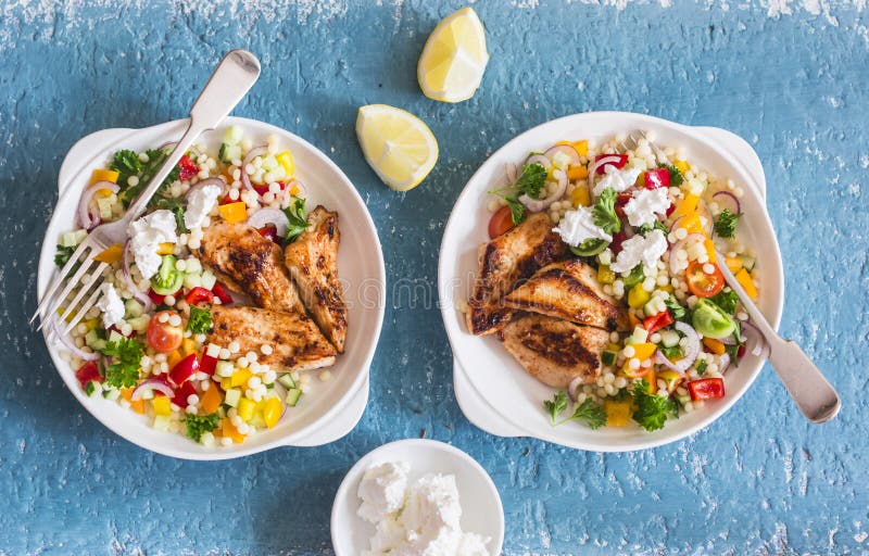 Le yaourt mariné a grillé le blanc de poulet et le couscous et la salade israéliens de tabouli de légumes sur un fond bleu images libres de droits Le yaourt mariné a grillé le blanc de poulet et le couscous et la salade israéliens de tabouli de légumes sur un fond bleu images libres de droits