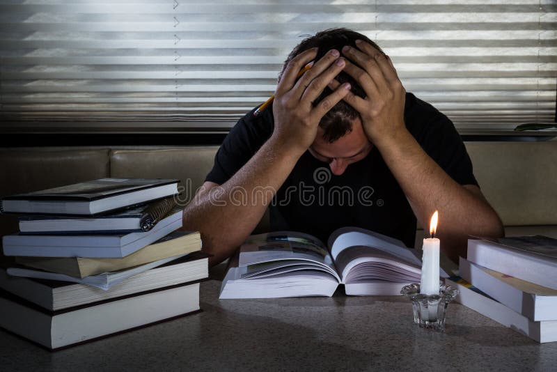 Giovani frustrati uomo con un libro aperto e molte altre chiusi libri a studiare a lume di candela.