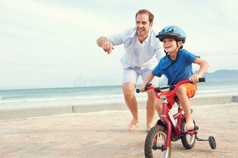 Father and son learning to ride a bicycle at the beach having fun together. Father and son learning to ride a bicycle at the beach having fun together