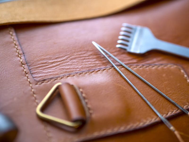 Leather craft or leather working. Selected pieces of beautifully colored or  tanned leather on leather craftman's work desk . Piece of hide and working  tools on a work table. Stock Photo