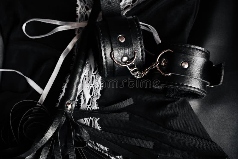 Lace sexy black womens underwear and set of erotic toys for BDSM. The game  of sexual slavery with a whip, handcuffs and leather mask on a light pink b  Stock Photo 