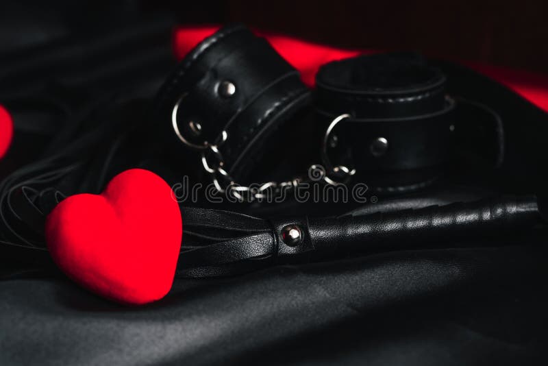 Leather whip and handcuffs for BDSM sex with red hearts as a symbol of Valentine`s day holiday with love and sex with submission