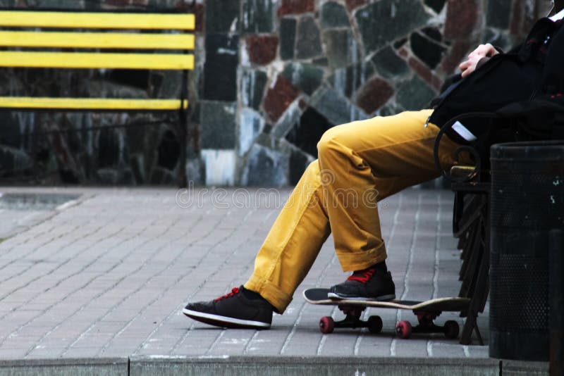 Lebensstil entspannen sich Hippie-Konzept Mann-Skateboardfahrer in den gelben Jeans, die auf Bank sich entspannen Gelbe Bank und stockfotografie Lebensstil entspannen sich Hippie-Konzept Mann-Skateboardfahrer in den gelben Jeans, die auf Bank sich entspannen Gelbe Bank und stockfotografie