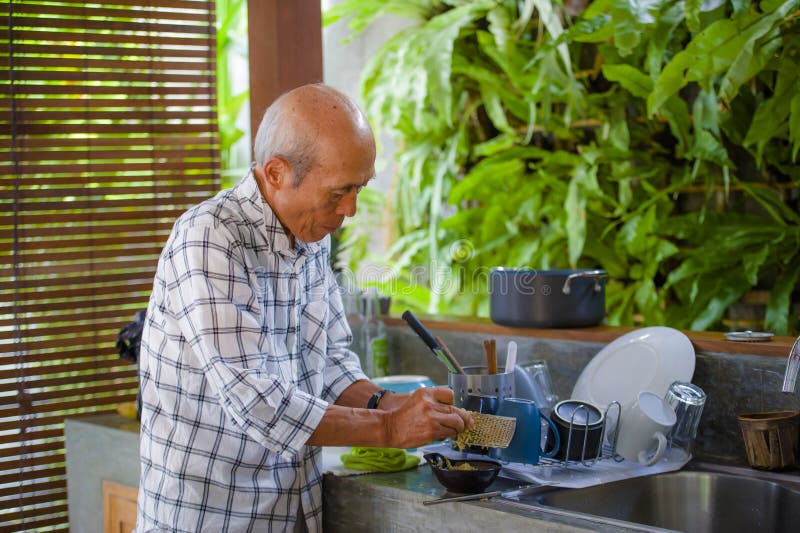 Lebensstilporträt des älteren glücklichen und süßen asiatischen japanischen Mannes im Ruhestand, der zu Hause die Küche allein or