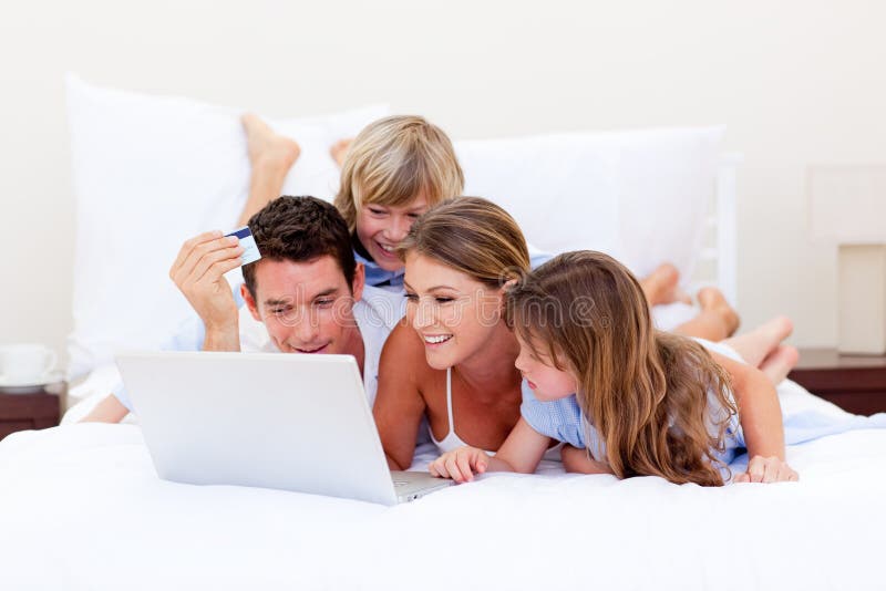 Lebhafte Familie, die online sich hinlegen auf Bett kauft