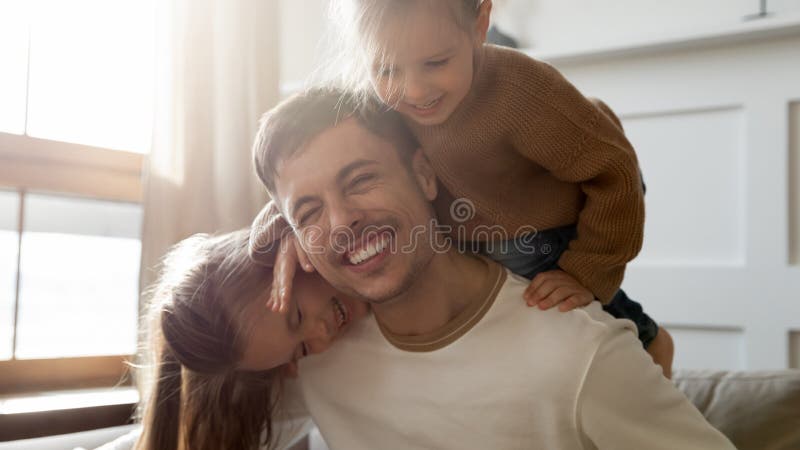 Lebhafte Töchter tragen den liebenden Vater angehängt, die zusammen im Wohnzimmer spielt lizenzfreie stockfotografie