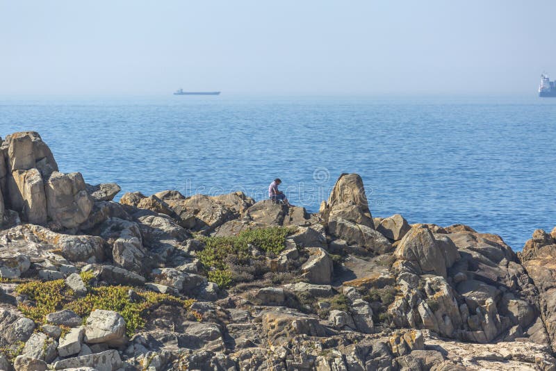Man enjoying the view, sitting on the rocks, next to the beach of Leca da Palmeira, background with ocean and ships royalty free stock images Man enjoying the view, sitting on the rocks, next to the beach of Leca da Palmeira, background with ocean and ships royalty free stock images