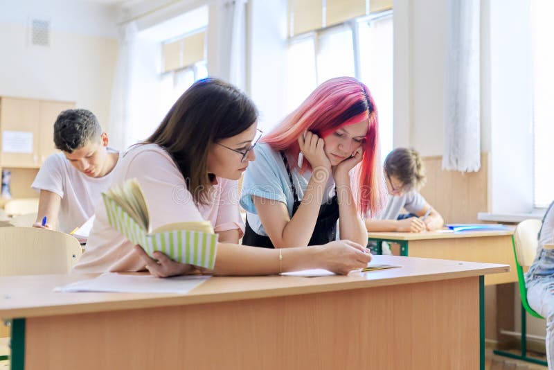 Lección en clase de estudiantes de secundaria profesora sentada en el escritorio con estudiante fotos de archivo