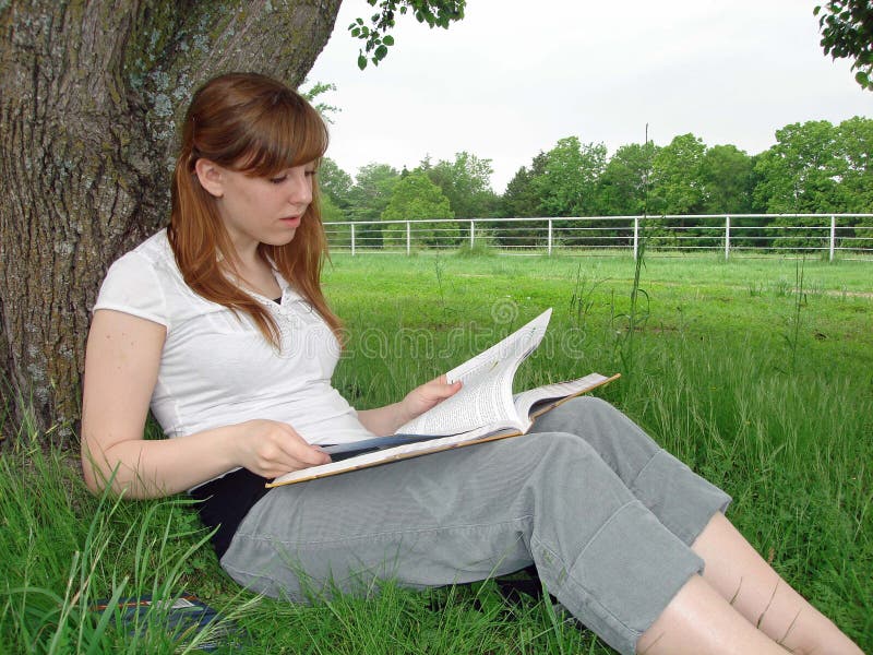 A teenage girl reads by a tree. A teenage girl reads by a tree.