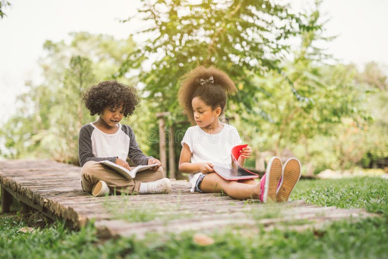 Little Afro child girl reading book between green spikes meadow garden with friend read education concept. Little Afro child girl reading book between green spikes meadow garden with friend read education concept