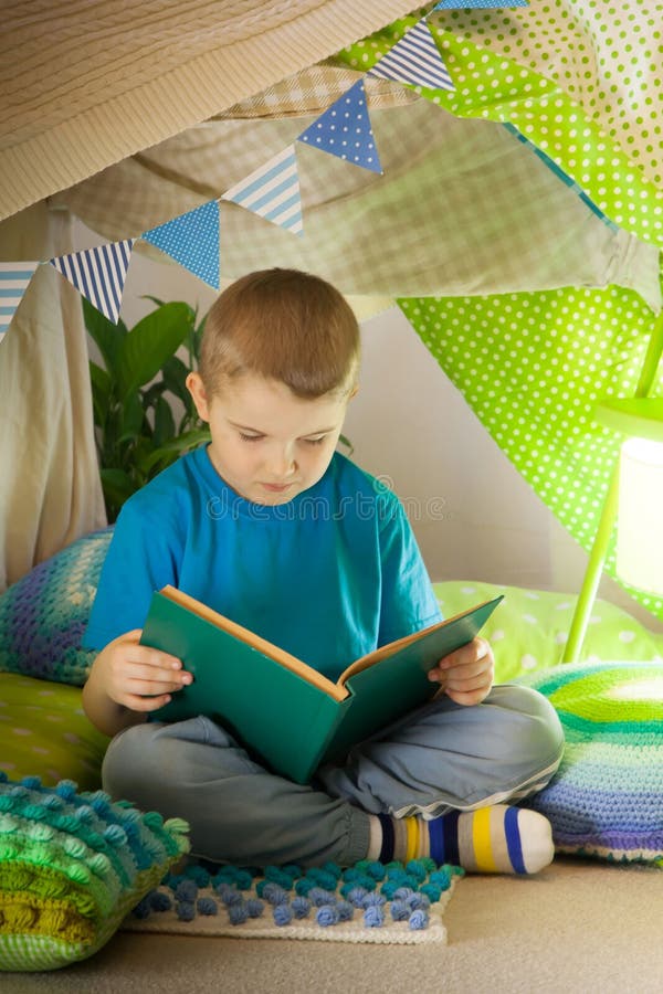 Lecture et jeux en famille sous la tente des enfants Garçon avec un livre avant d'aller au lit image stock Lecture et jeux en famille sous la tente des enfants Garçon avec un livre avant d'aller au lit image stock