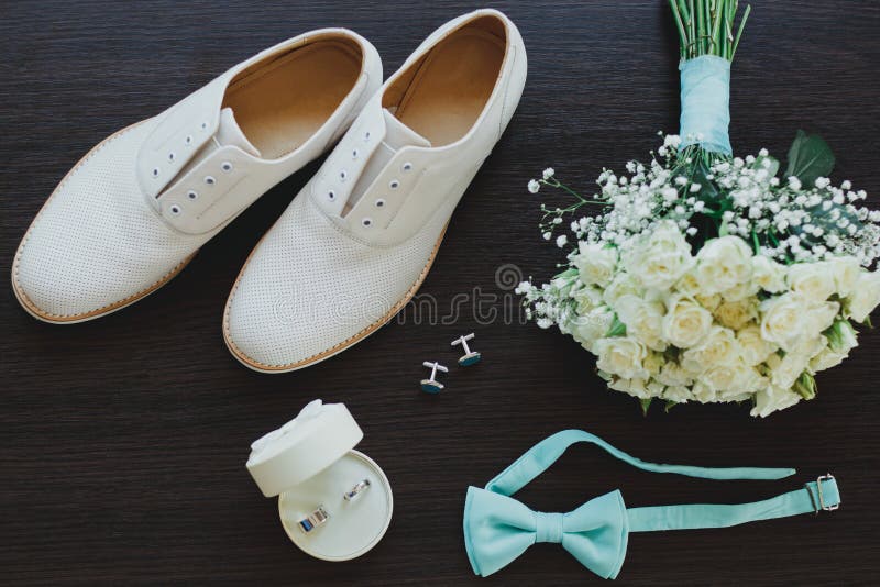Lederne weiße Bräutigamhochzeitsschuhe auf dem hölzernen Hintergrund in den Sonnenstrahlen Ringe, Fliege und Manschettenknöpfe mi lizenzfreies stockbild Lederne weiße Bräutigamhochzeitsschuhe auf dem hölzernen Hintergrund in den Sonnenstrahlen Ringe, Fliege und Manschettenknöpfe mi lizenzfreies stockbild