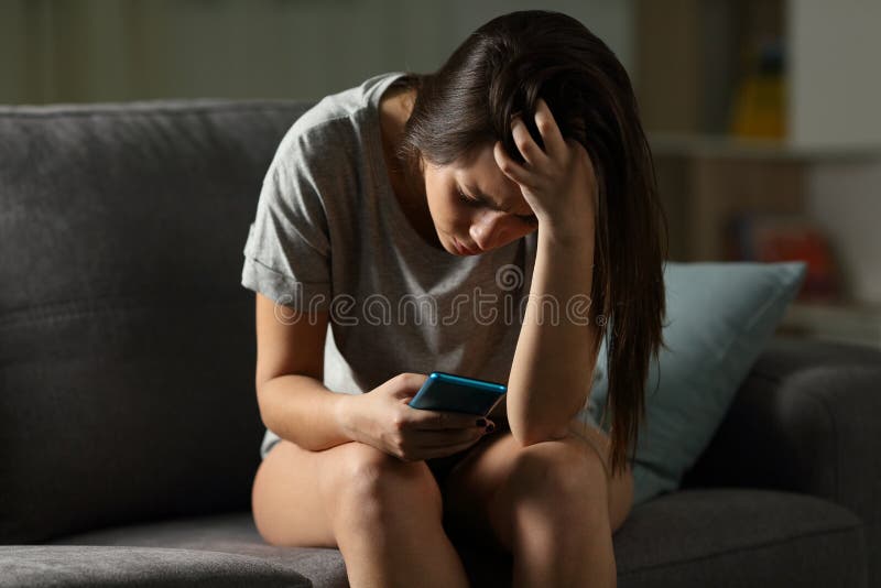 Sad teen being victim of cyber bullying online sitting on a couch in the living room at home. Sad teen being victim of cyber bullying online sitting on a couch in the living room at home