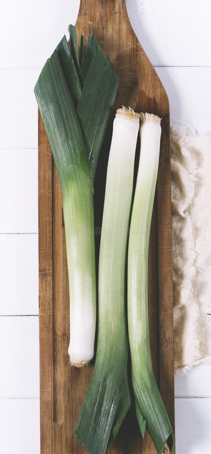 Leek on light textiles and cutting board on a white background the aged wooden planks of vintage vertical top view stock photo Leek on light textiles and cutting board on a white background the aged wooden planks of vintage vertical top view stock photo