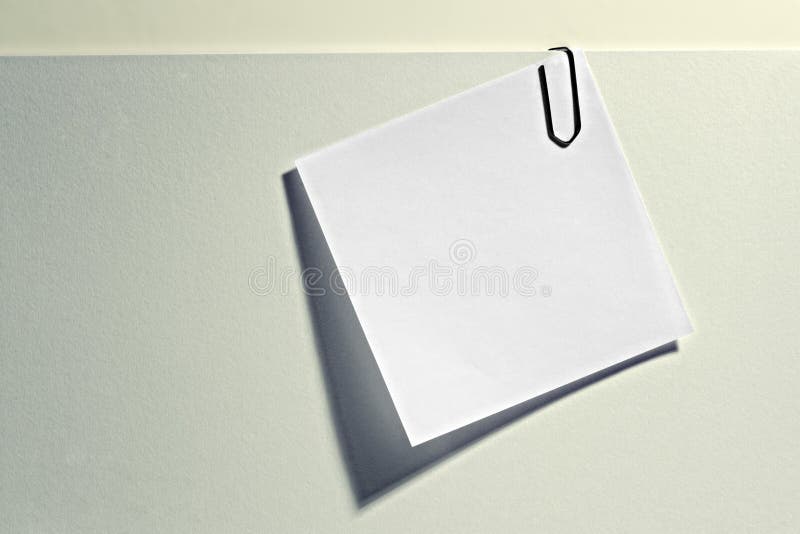 Small white blank notelet attached to a larger light grey document with a paperclip for your memo, reminder or addendum. Small white blank notelet attached to a larger light grey document with a paperclip for your memo, reminder or addendum