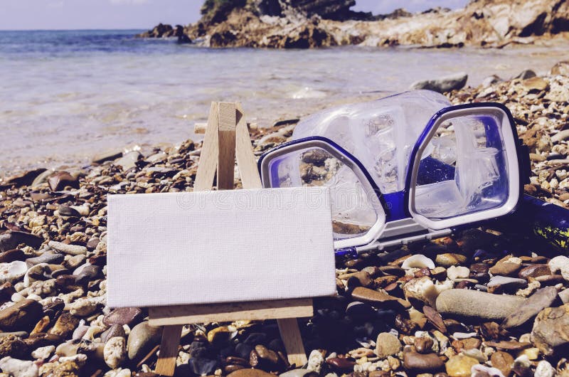 Leerer weißer Segeltuchrahmen mit Gestell auf dem Strand Taucherbrille und Schnorchel-Gang auf dem Stein lizenzfreies stockfoto Leerer weißer Segeltuchrahmen mit Gestell auf dem Strand Taucherbrille und Schnorchel-Gang auf dem Stein lizenzfreies stockfoto